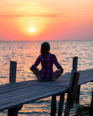 girl is sitting in lotus pose on an old wooden pier and enjoys the sunset on the sea