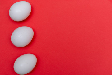 Three Easter holiday flat lay with white egg on a solid bright red vibrant background with copy space on right.
