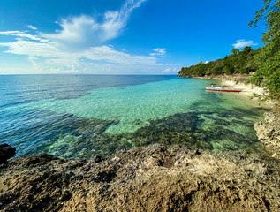 Amazingly beautiful landscape of a rocky coast background a transparent turquoise sea and a blue sky with white clouds. A boat near the shore of a sandy beach near the trees.