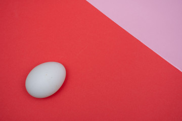 Fototapeta na wymiar Easter holiday flat lay with white egg on a solid bright red and pink vibrant background with copy space.