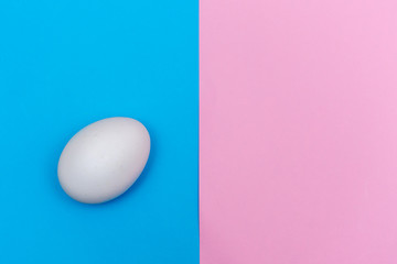 Easter holiday flat lay with white egg on a solid bright blue and pink vibrant and pastel background with copy space.