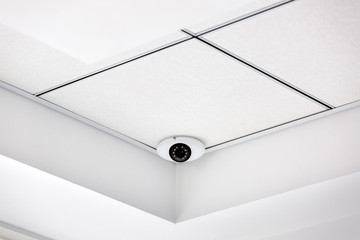 CCTV camera in the corner on a white suspended ceiling, security system close up.