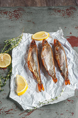 Smoked capelin and smelt on white paper close-up with lemon and fragrant herbs