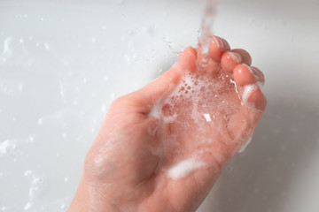 Washing hand over the sink in the bathroom under water stream with soap foam, close-up. Concept healthcare and hygiene