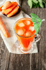 Delicious and fresh carrot juice with mint and lettuce leaves. Chilled vegetable smoothie with ice in a glass glass. Close up.