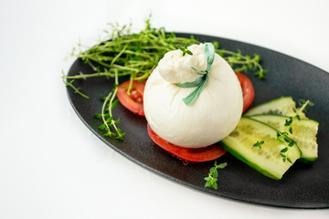 fresh Italian burrata cheese with tomato slices on a black plate on a white background. Selective focus.
