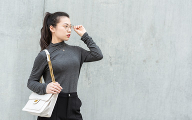 Urban young woman leaning on gray wall with shoulder bag