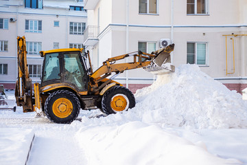 Snow removal equipment on the road in winter. Yellow excavator removes a huge mountain of snow....