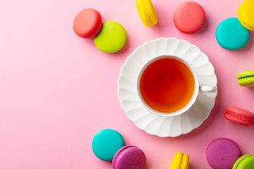 Macaroons dessert and cup of tea on pink background. Copy space. Top view.