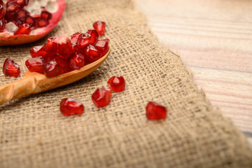 Chunks of ripe juicy pomegranate and pomegranate seeds on a wooden spoon on a background of rough homespun fabric. Close up.
