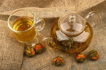Flower tea brewed in a glass teapot, a glass of tea and balls of flower tea on a background of rough homespun fabric. Close up.
