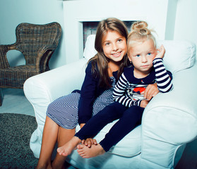 two cute sisters at home playing, little smiling girl in house interior on sofa, messing hair,...