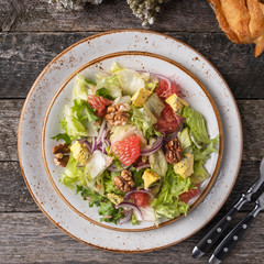 Diet salad with garpefruit, cheese, lettuce and walnut on a plate served with fork and knife. Top view