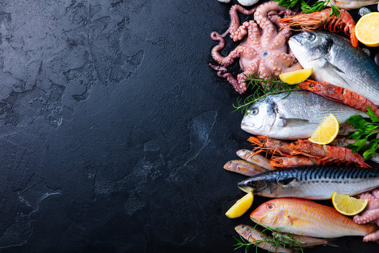 Fresh raw fish and seafood assortment on black slate background. Top view. Copy space.