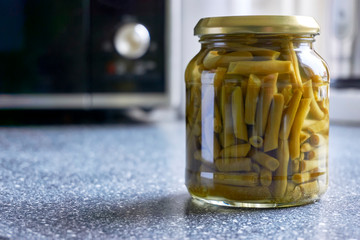 Single glass jar with canned green beans on kitchen top with microwave. Image with copy space and...