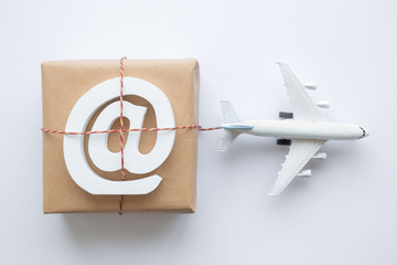 Cardboard delivery box with e-mail sign and small airplane abstract on white.