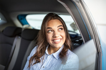 Businesswoman in car on the way to her workplace. Beautiful girl in the backseat. Beautiful businesswoman is sitting on back seat of the car. She is looking through the window dreamingly and smiling.