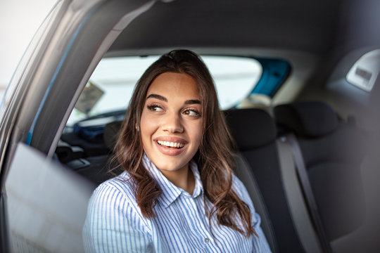 Businesswoman in car on the way to her workplace. Beautiful girl in the backseat. Beautiful businesswoman is sitting on back seat of the car. She is looking through the window dreamingly and smiling.