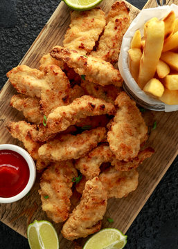 Buttermilk Chicken Nuggets Served On Wooden Board With Potato Chips, Lime Wedges And Tomato Ketchup