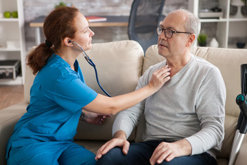 Obraz premium Pretty female nurse using stethoscope to listen the heart of old man
