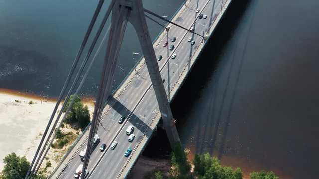 Drone glight over large bridge with traffic cars and vehicles driving to their destination on highway passing-by. Beautiful city river and urban landscape.