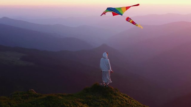 Young girl with kite standing on top of mountain amazing view outdoor woman happiness happy landscape hiking sky meadow grass sunlight free travel relax active wind slow motion