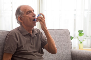 Senior man taking an inhaler at home. (Health and fitness) - obrazy, fototapety, plakaty