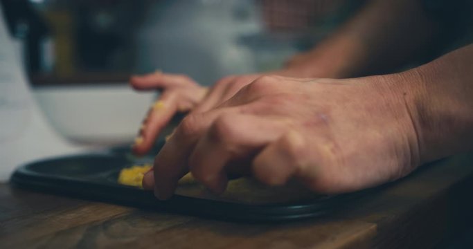 Hands of young woman pushing dough into cookie tray