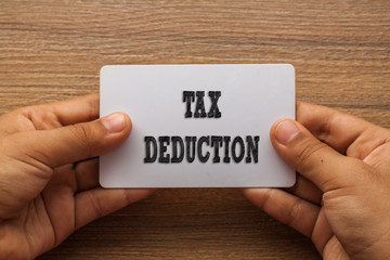 TAX DEDUCTION written on card with hand holding it with wood background