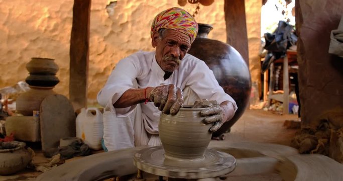 Indian potter at work: throwing the potter's wheel and shaping ceramic vessel and clay ware: pot, jar in pottery workshop. Experienced master. Handwork craft from Shilpagram, Udaipur, Rajasthan, India