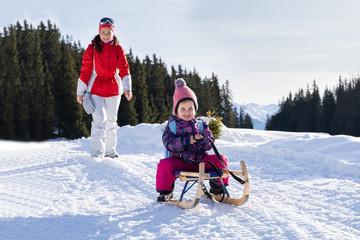 Girl Enjoying Sledding With Her Mother Against Winter Forest