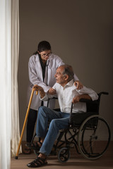 Senior man trying to get up from the wheelchair with the help of a doctor. (Health and fitness) 
