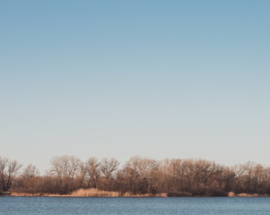 Landscape with river and trees in winter. Bright blue sky without clouds above river.