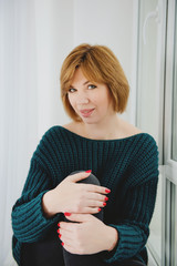 Portrait of a red-haired girl who is sitting on the windowsill.