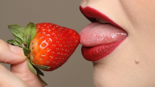 Woman imitates masturbation. Sensual red lips is licking strawberry. Sexy woman's tongue and lips