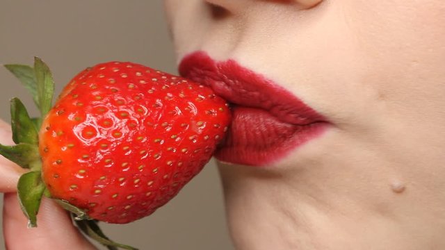 Woman imitates masturbation. Sensual red lips is licking strawberry. Sexy woman's tongue and lips