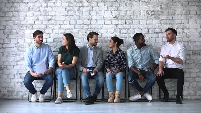 Friendly multiethnic business people chatting sit on chairs in row