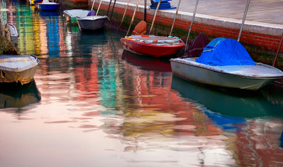 Fototapeta na wymiar Colorful reflection in canal water of anchored motor boats and painted in vibrant colors houses' facades in Burano, Italy.