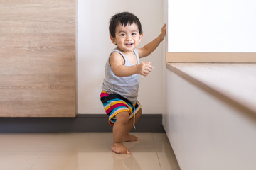 Cute active asian little baby boy is standing on the floor and trying begin to walk for first step himself, concept of learning and developing of child in the first year of life.