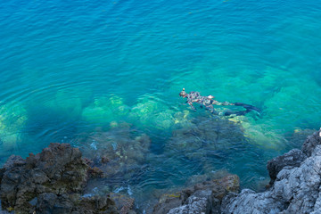 Spear fishing diver top view in green blue waters near rocks