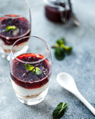 Two layered dessrts in glasses with granola, yogurt and berry jam