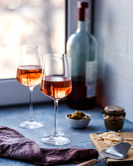 Two glasses of rose wine on a blue background whith sliced cheese an olives