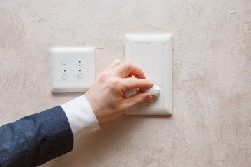 Man regulating temperature on air conditioning controller thermostat on the wall