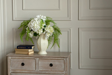 A white house with white flowers stands on the dresser against the wall.