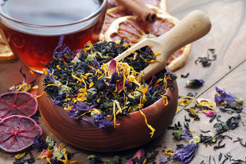 blended tea. black tea with dry flower petals and citrus fruits. dry black tea leaves in a wooden...