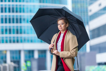 Rain. Outdoors lifestyle fashion portrait of stunning brunette girl. Walking on the city street. Going shopping. Wearing stylish white fitted coat, red neckscarf, black umbrella cane. Business woman.