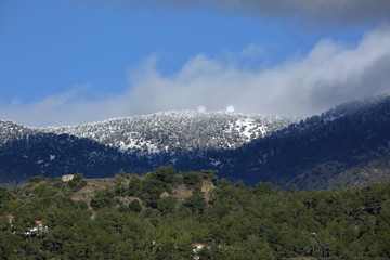 Trodos mountains under snow seen from valley, blue sky with heavy gray clouds, Cyprus