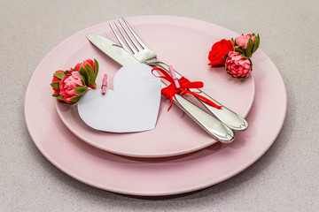 Romantic table setting on light stone concrete background. Valentine's day or Wedding card template. Paper heart, flowers, cutlery