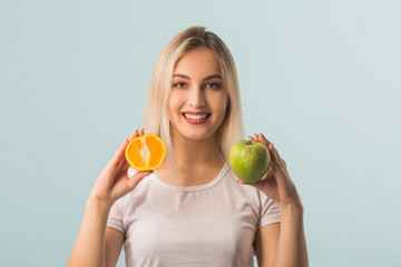 beautiful young woman with green apple and orange in hands on a blue background