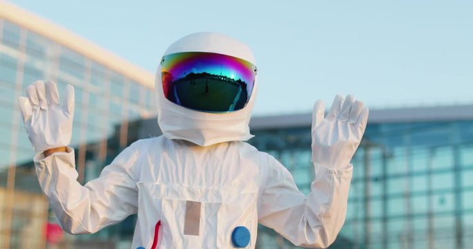 Portrait of the man or a woman in the full costume of astronaut with head armor waving with hands to the camera before going to the outer space in a rocket. Outdoors.